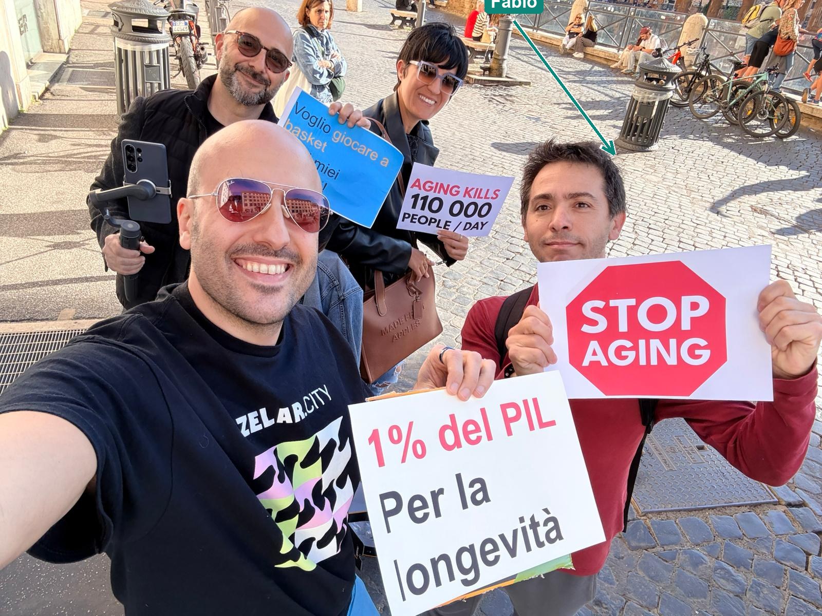 Participants at the Fund Longevity rally in Rome holding signs reading STOP AGING, AGING KILLS 110,000 PEOPLE/DAY and 1% del PIL per la longevità
